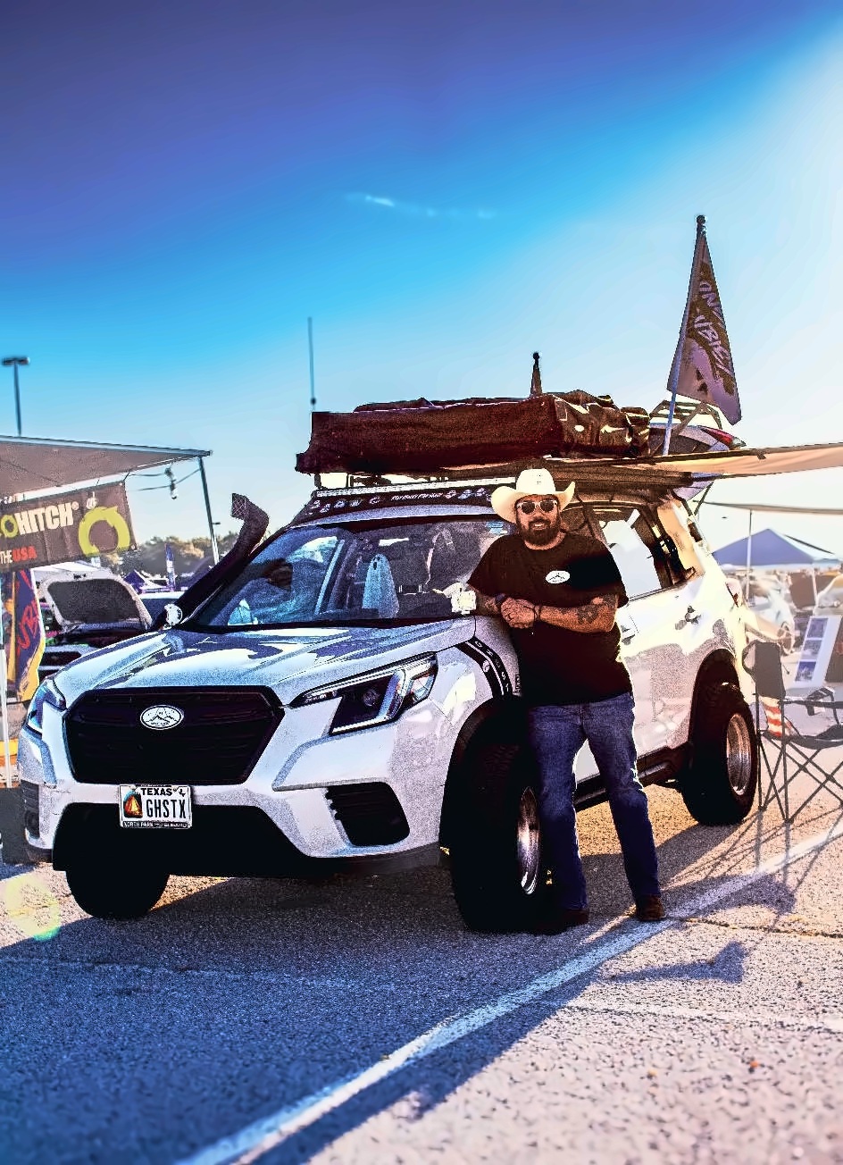 Roman leaning on the Ghost with the rooftop tent and awning deployed at an event